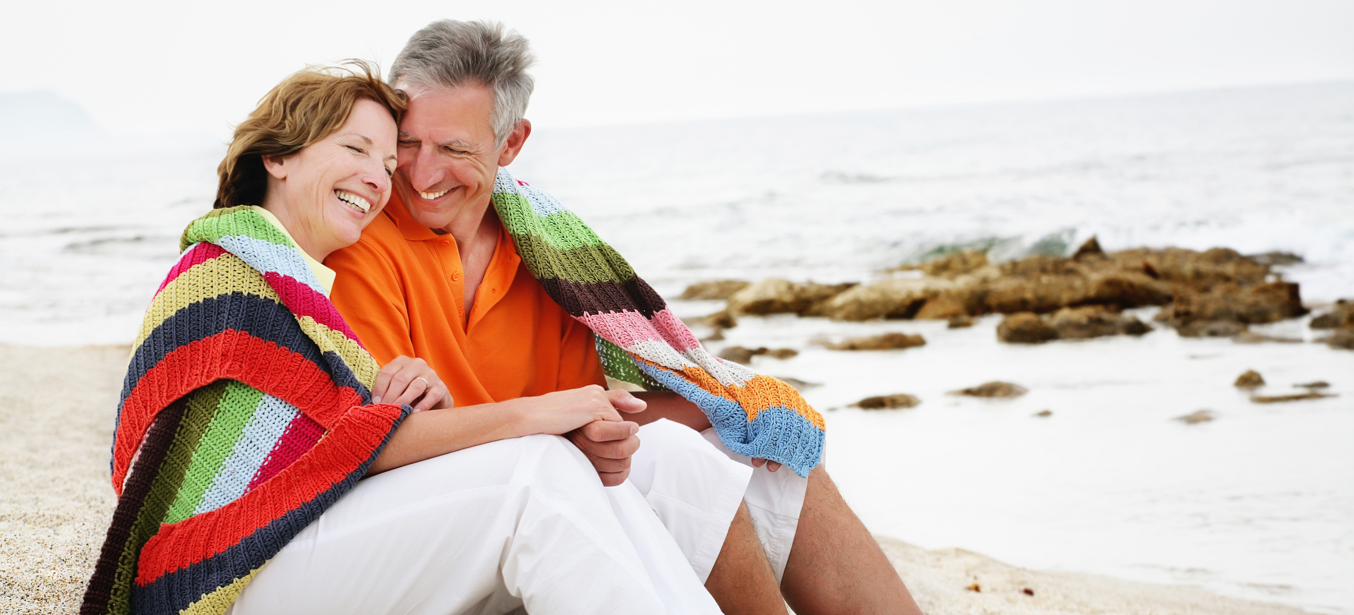 Middle-aged couple sitting on a beach enjoying each others company. 