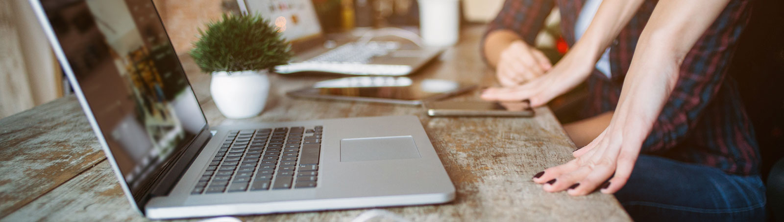 Two sets of hands in front of two laptops on wooden table