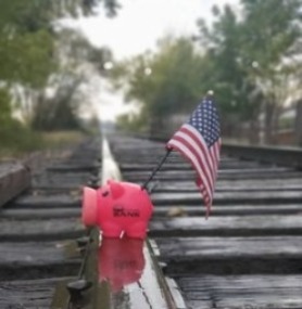 Piggy bank on railroad tracks with American flag in it
