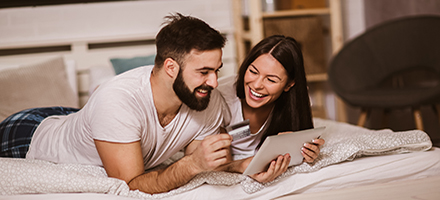 Couple laying on bed looking at tablet with debit card in hand