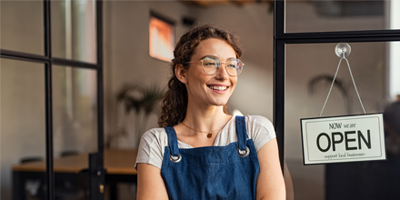 Happy business owner standing in front of open sign looking into the distance