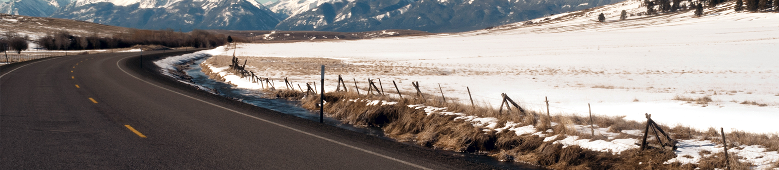 Road next to snowy field with mountain range in the background