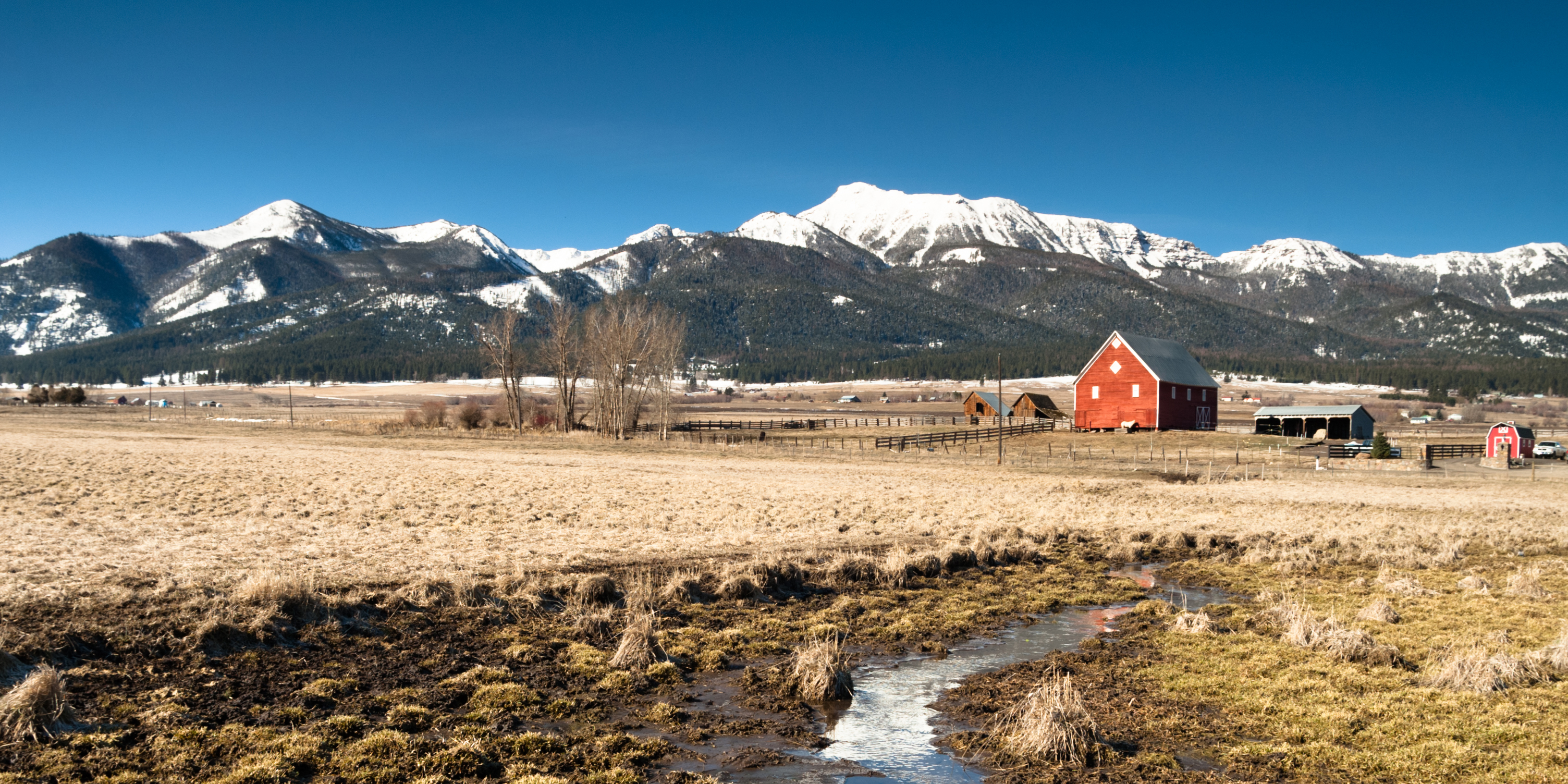 Red barn at the foot of large mountain range.