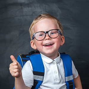 Young boy with backpack holding a thumbs up.
