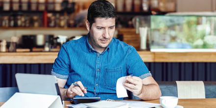 Restaurant owner calculating finances on laptop and calculator