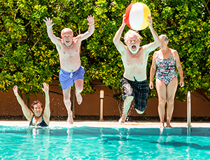 Senior citizens jumping into pool with beach ball.