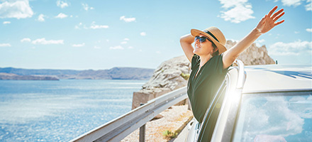 Woman hanging out of car window looking at the sea.