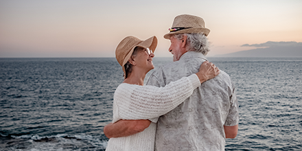 Senior couple smiling at each other with ocean in the background. 